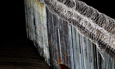 Photo of a boy looking at the border wall topped with razor wire
