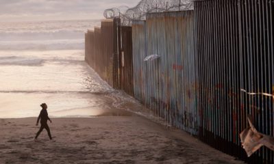 Photo of a woman walking along the beach next to the border wall in Mexico