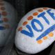 Photo of a stone painted with the word "VOTE" painted on it