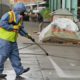 Photo of a city worker cleaning the sidewalk by a tent city