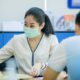 Image of a woman in a bank wearing a COVID-19 mask across from a customer